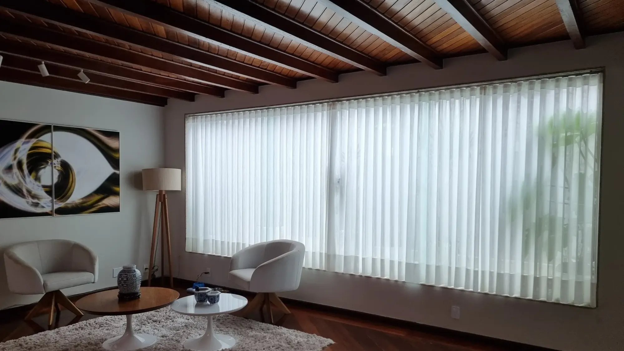 Sala com persiana vertical em janela ampla e teto de madeira